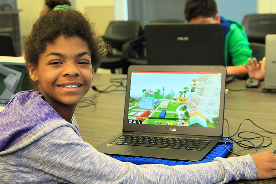 middle school student smiling while programming on laptop computer