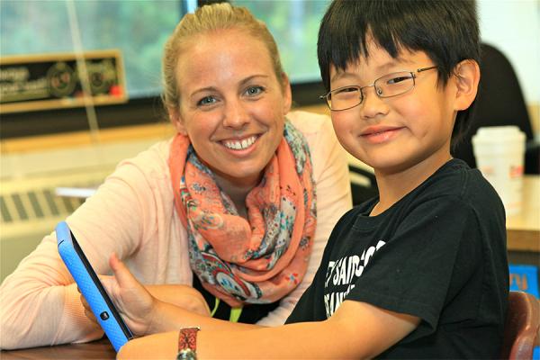 teacher and young boy with ipad smiling at camera