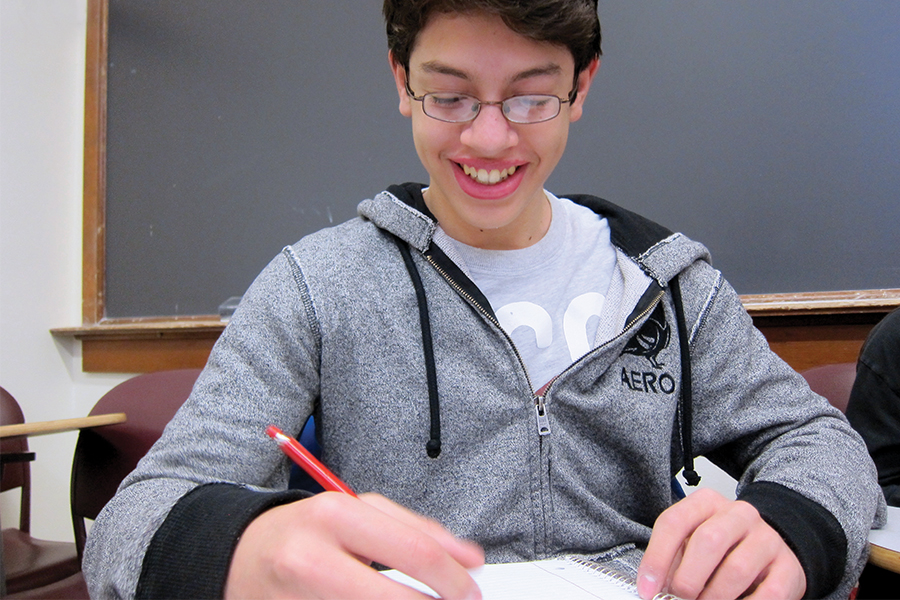 "middle school boy in a classroom taking a test at a desk"