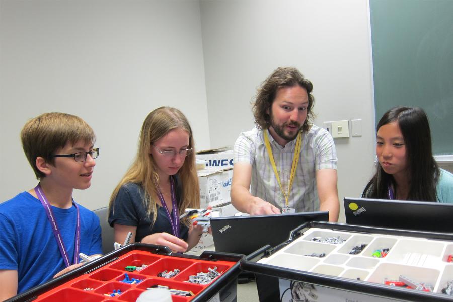 male teacher with three middle school students teaching robotics