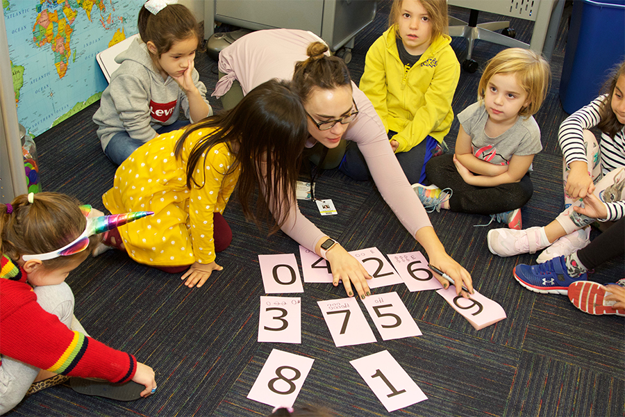 group of early childhood students playing math game on floor with teacher