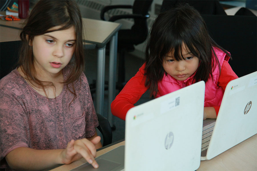 two young girls working on laptop computers
