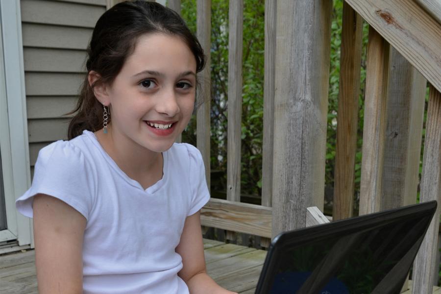 elementary school girl working on her laptop on porch stairs