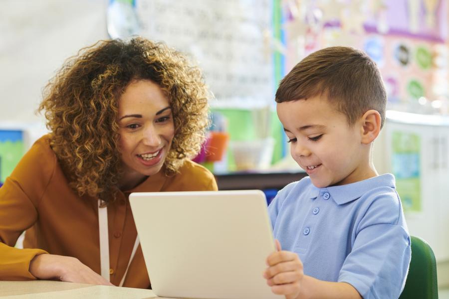 young boy working with adult teacher on iPad