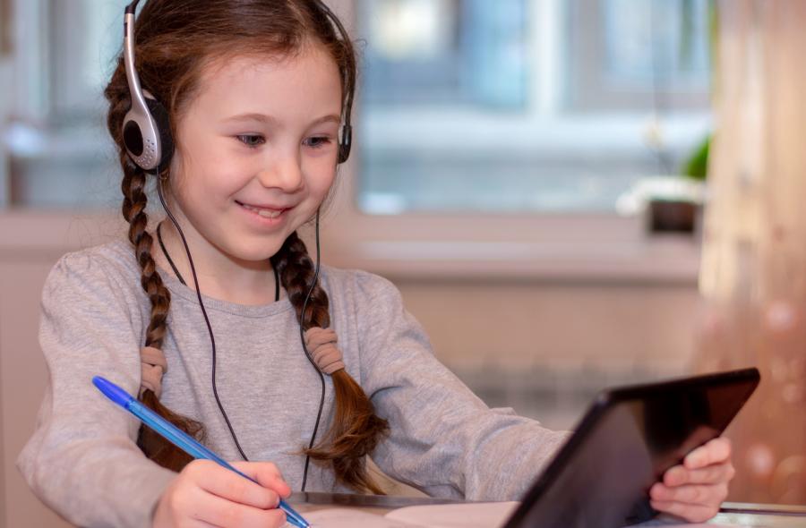 elementary school girl with braids in headphones on tablet