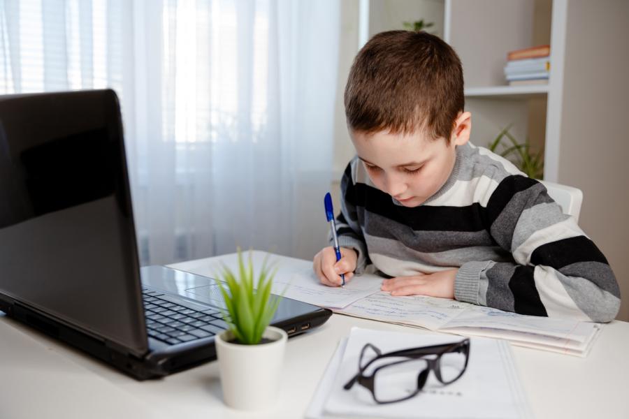 elementary school boy writing in front of a laptop
