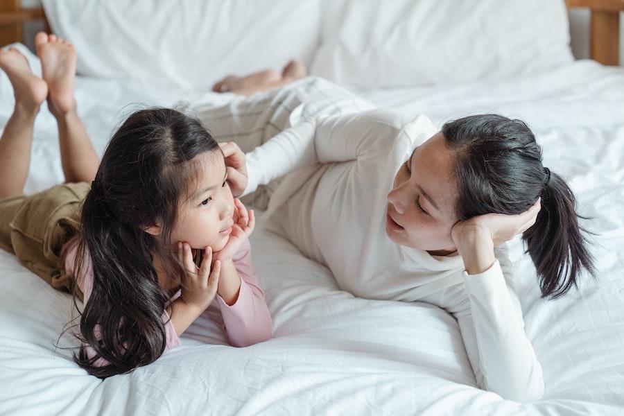 parent and young child talking on bed