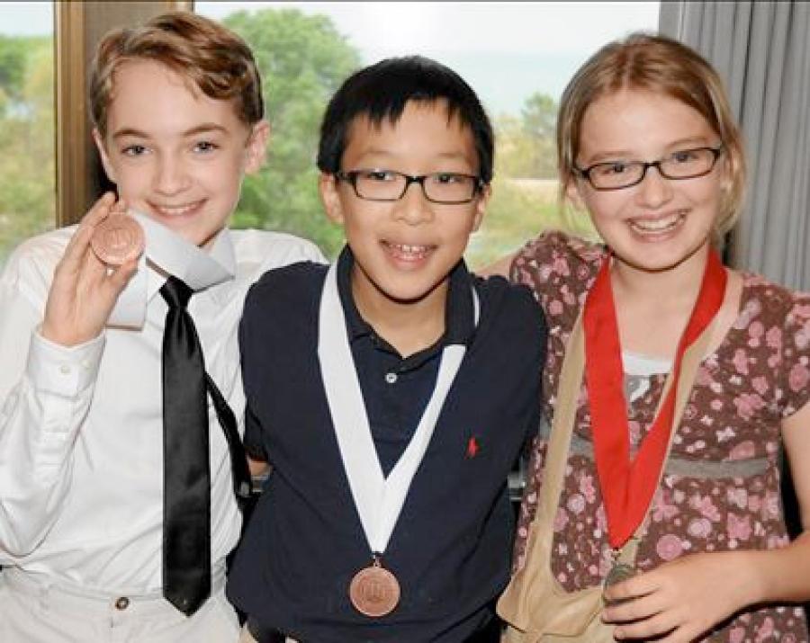 three middle school students at ceremony with medals