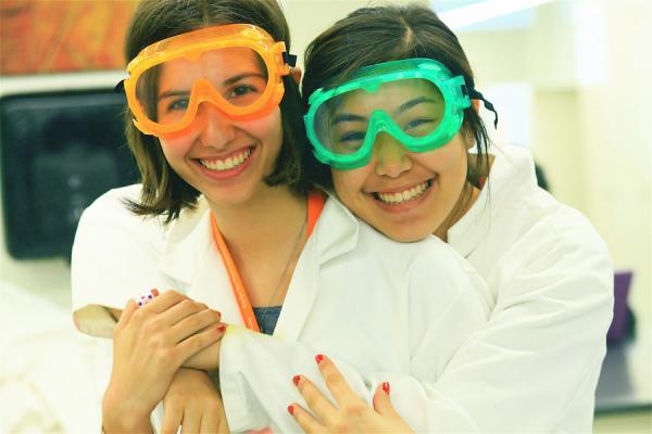 two high school girls in science lab gear embracing and smiling for camera