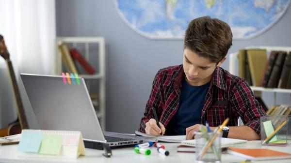 middle school boy taking notes in online course