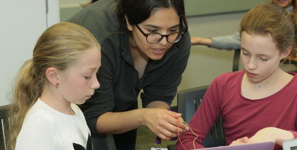 two girls with teacher working with electronics