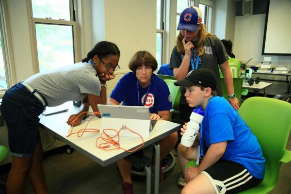 three middle school students working with teacher on computer programming